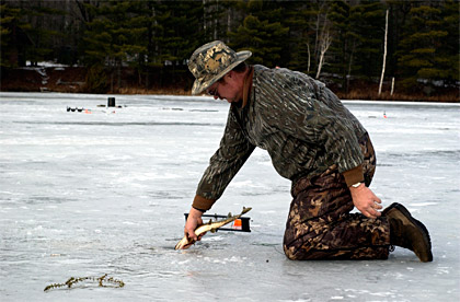 Ice fisherman releasing a small Northern Pike back through the ice